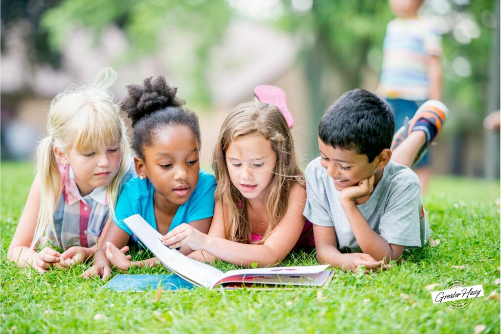 children laying down in the grass reading a book